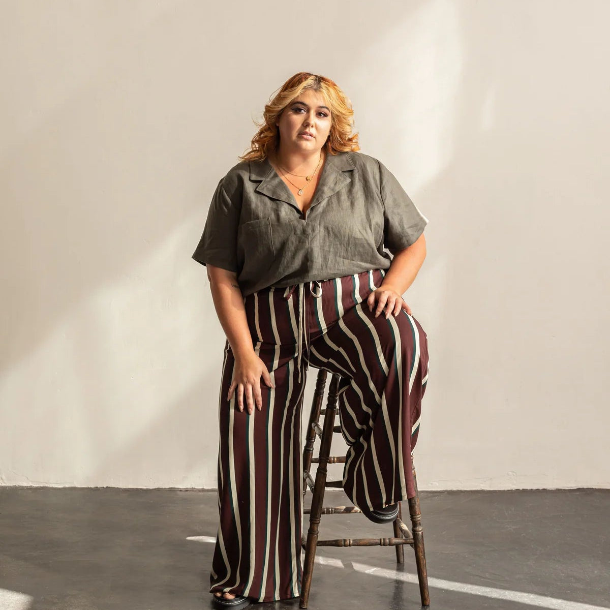 Woman sitting on a stool wearing a grey collared shirt