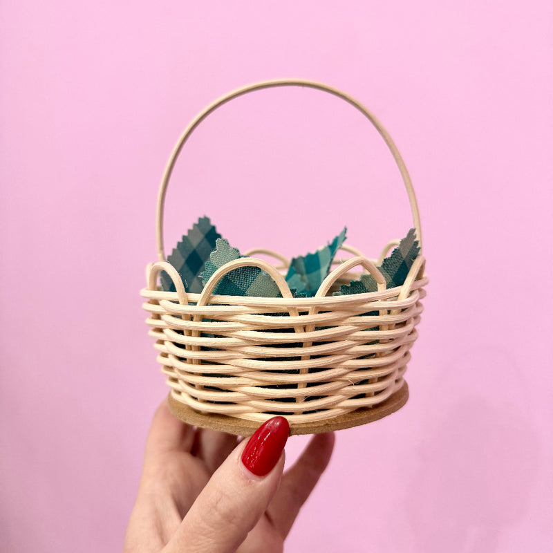Mini rattan basket held in front of a pink background.