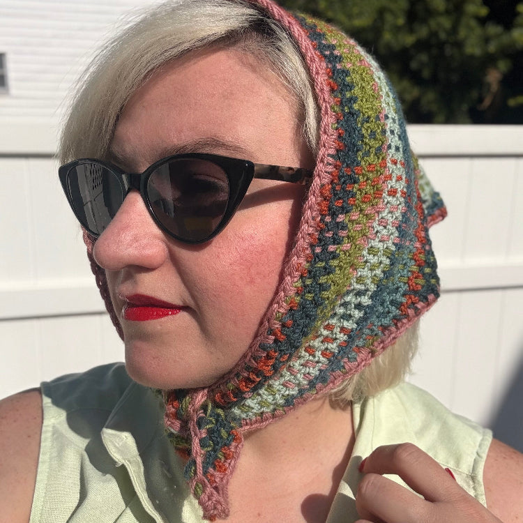 A woman with blonde hair wearing sunglasses and a plaid crochet kerchief tied under her chin.